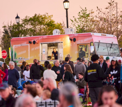 A crowd of people gathered around a food truck at dusk.