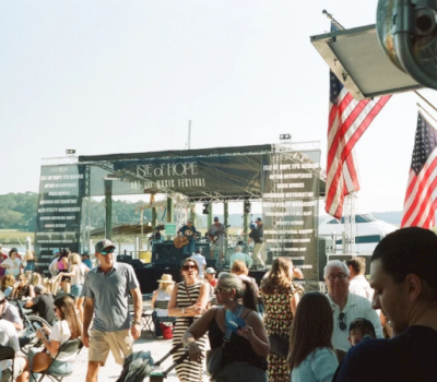 A crowd of people at an outdoor event with a stage and American flags.