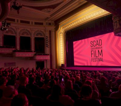 A large auditorium with a stage and screen showing an event