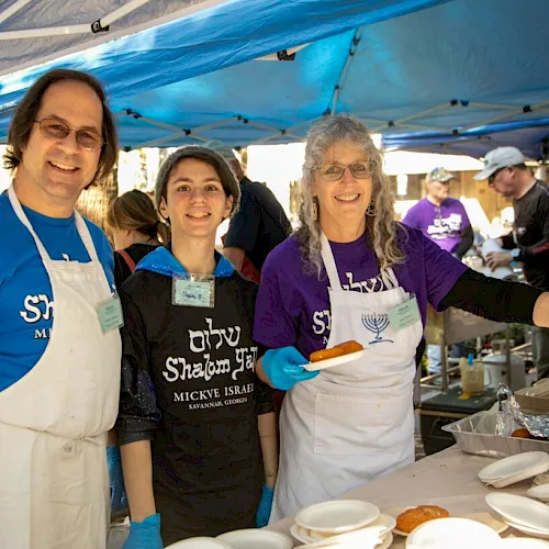 A food stall at an outdoor market with friendly cooks in aprons serving snacks under blue canopy tents.
