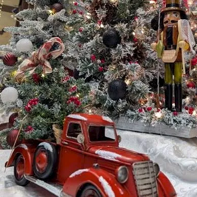 A festive Christmas display with a decorated tree, snowlike ornaments, and a nutcracker and toy red truck.