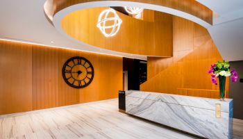 A modern lobby area with a marble reception desk, a large wall clock, unique light fixtures, and wooden wall paneling and decor.