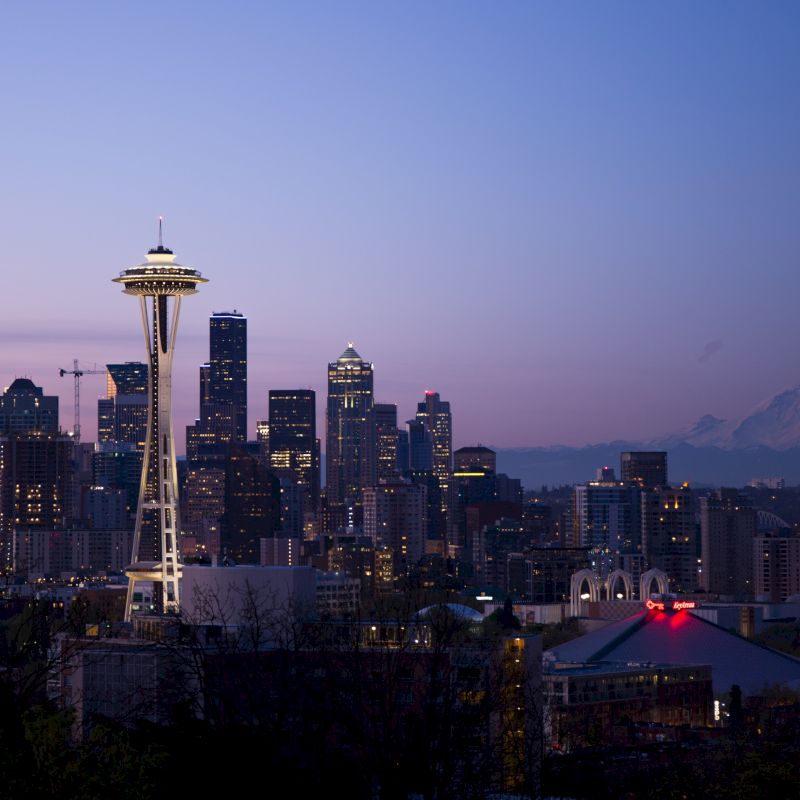 A cityscape featuring the Space Needle, downtown skyscrapers, and Mount Rainier in the background during dusk in Seattle, Washington.