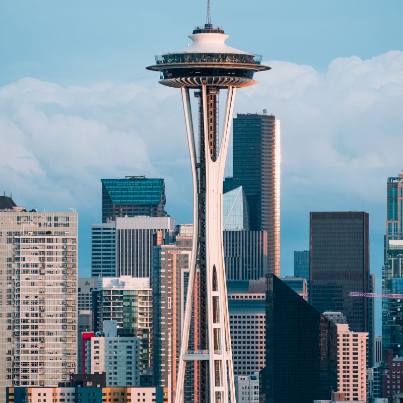 The image features the Space Needle in Seattle, Washington, with a backdrop of the city's modern skyscrapers and a partly cloudy sky.