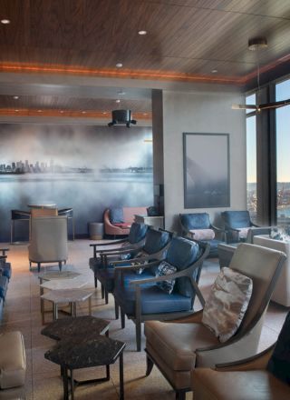 This image shows a modern lounge area with comfortable seating, large windows offering a scenic view of water and a ferris wheel in the background.
