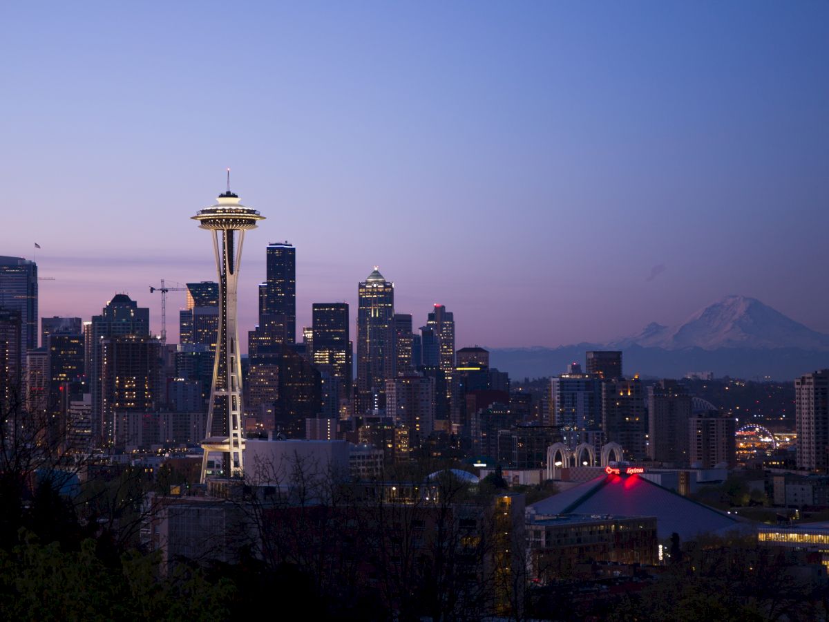 This image shows the Seattle skyline at dusk, featuring the Space Needle and various high-rise buildings, with Mount Rainier in the background.