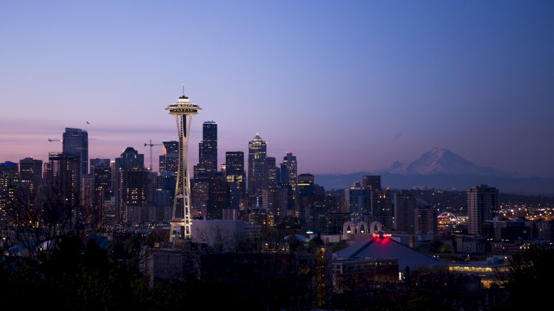 This image shows the Seattle skyline at dusk, featuring the Space Needle and various high-rise buildings, with Mount Rainier in the background.